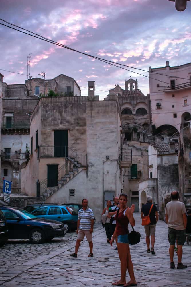 How to travel as a student: A girl exploring the narrow streets and elevated cave buildings in Matera, Italy during a colourful sunset