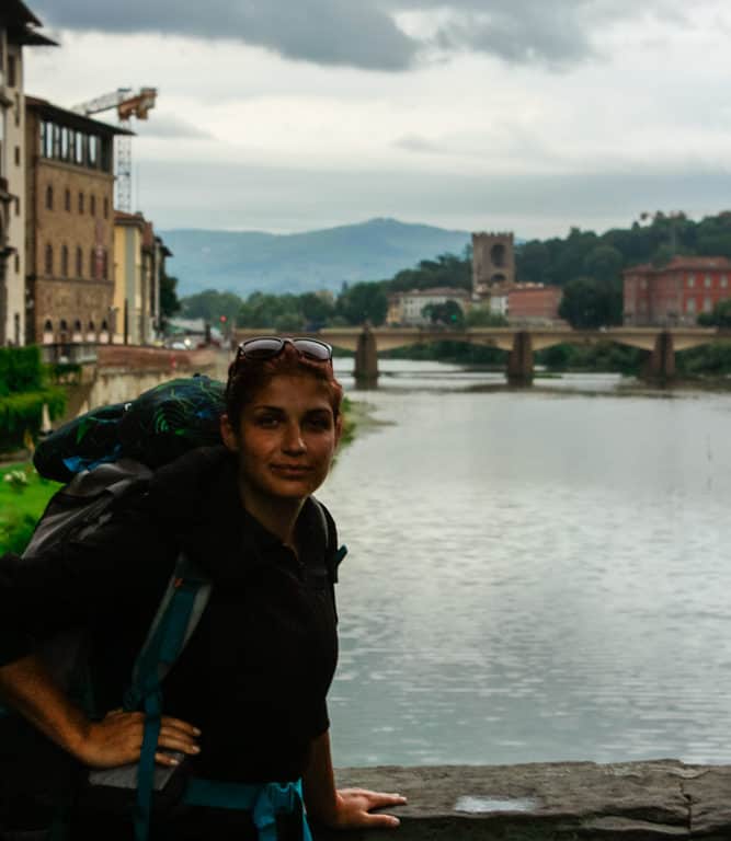 A travelling student with a backpack standing on a bridge on the Arno River in Florence, Italy