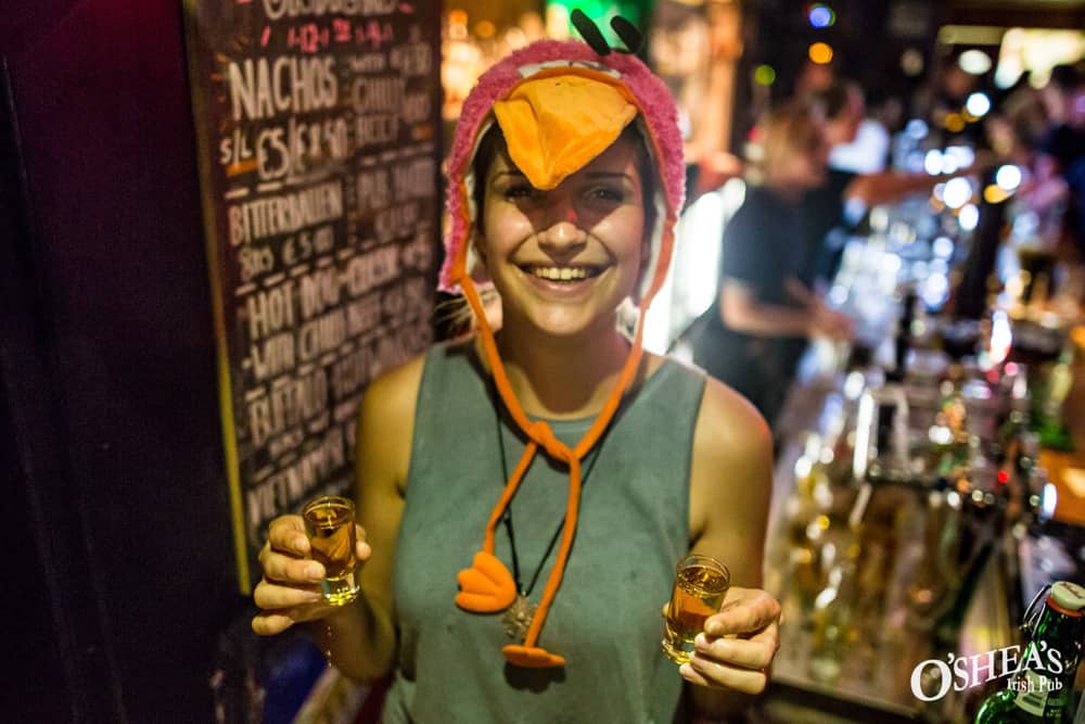 Earning money while studying, a smiling girl working in a busy bar, holding shot glasses in hand