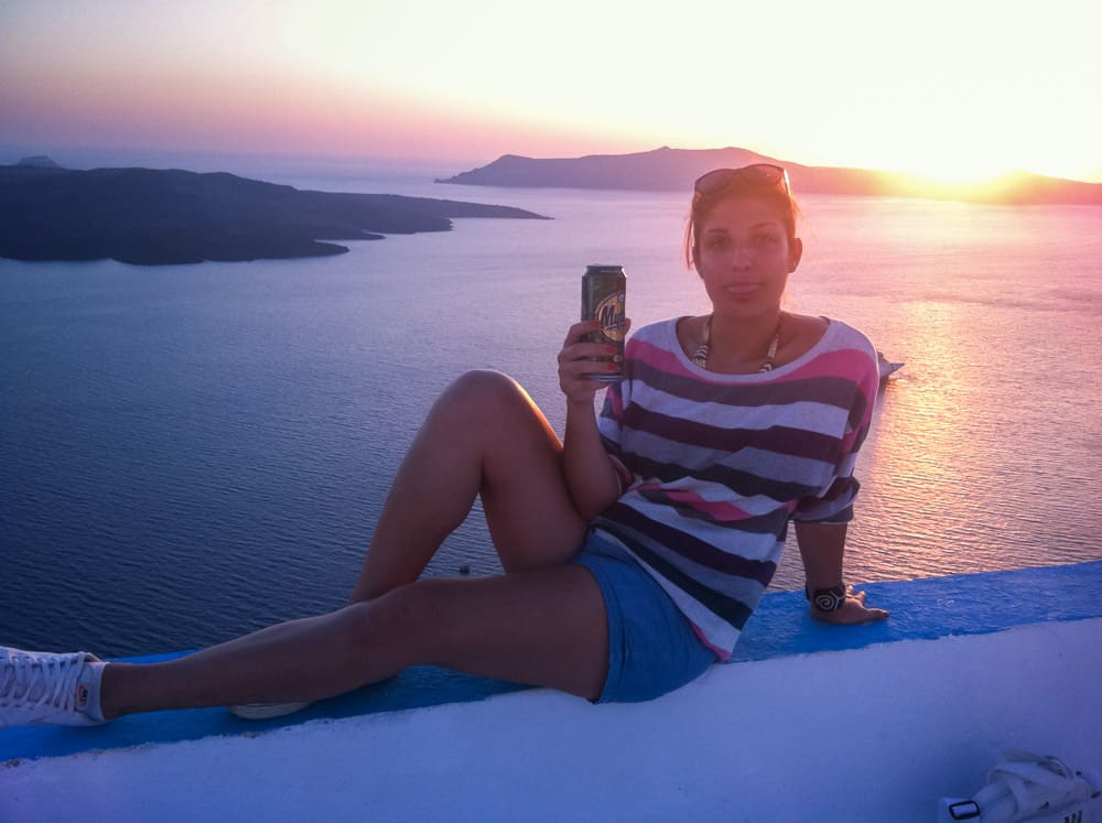 A girl enjoying a can of beer during a stunning pink sunset over the ocean in the island of Santorini in Greece