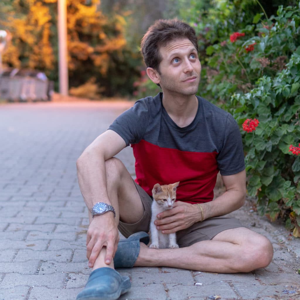 A man holding a cute kitten while sitting on the street