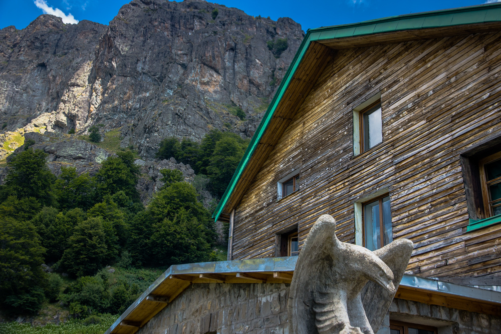 Stone eagle monument in front of the wooden Heavenly chalet and the high cliffs