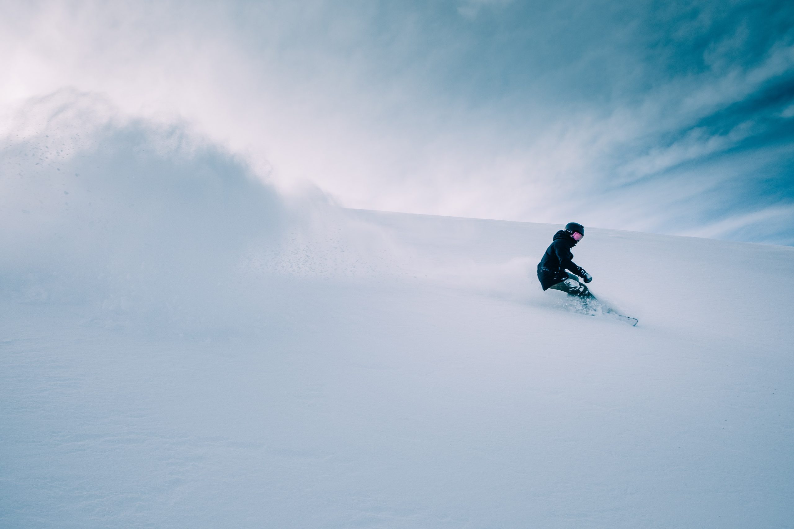 A man snowboarding in the mountain, leaving a huge trail of flying snow