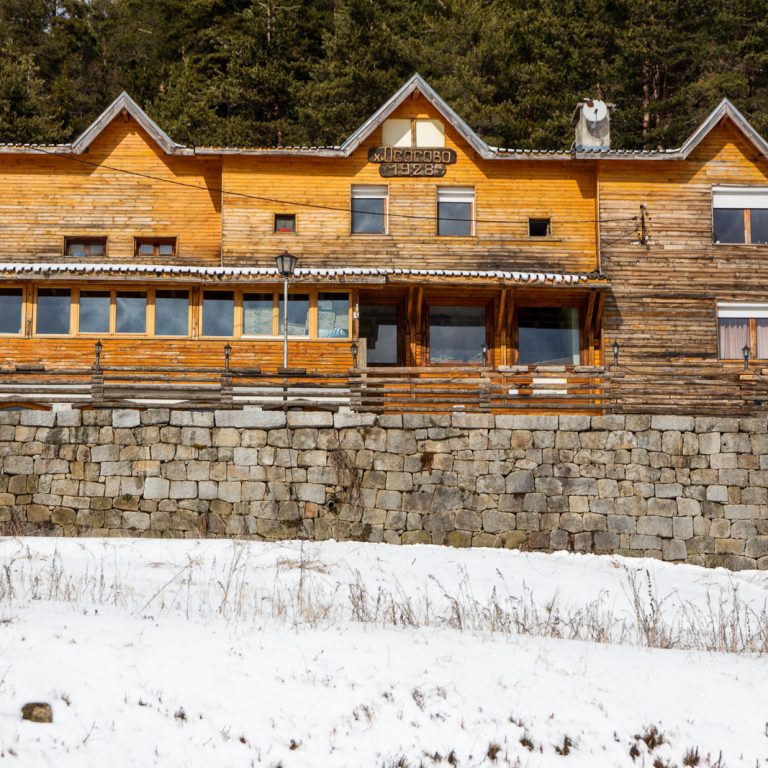 Wooden hut Osogovo with snow outside and a forest behind