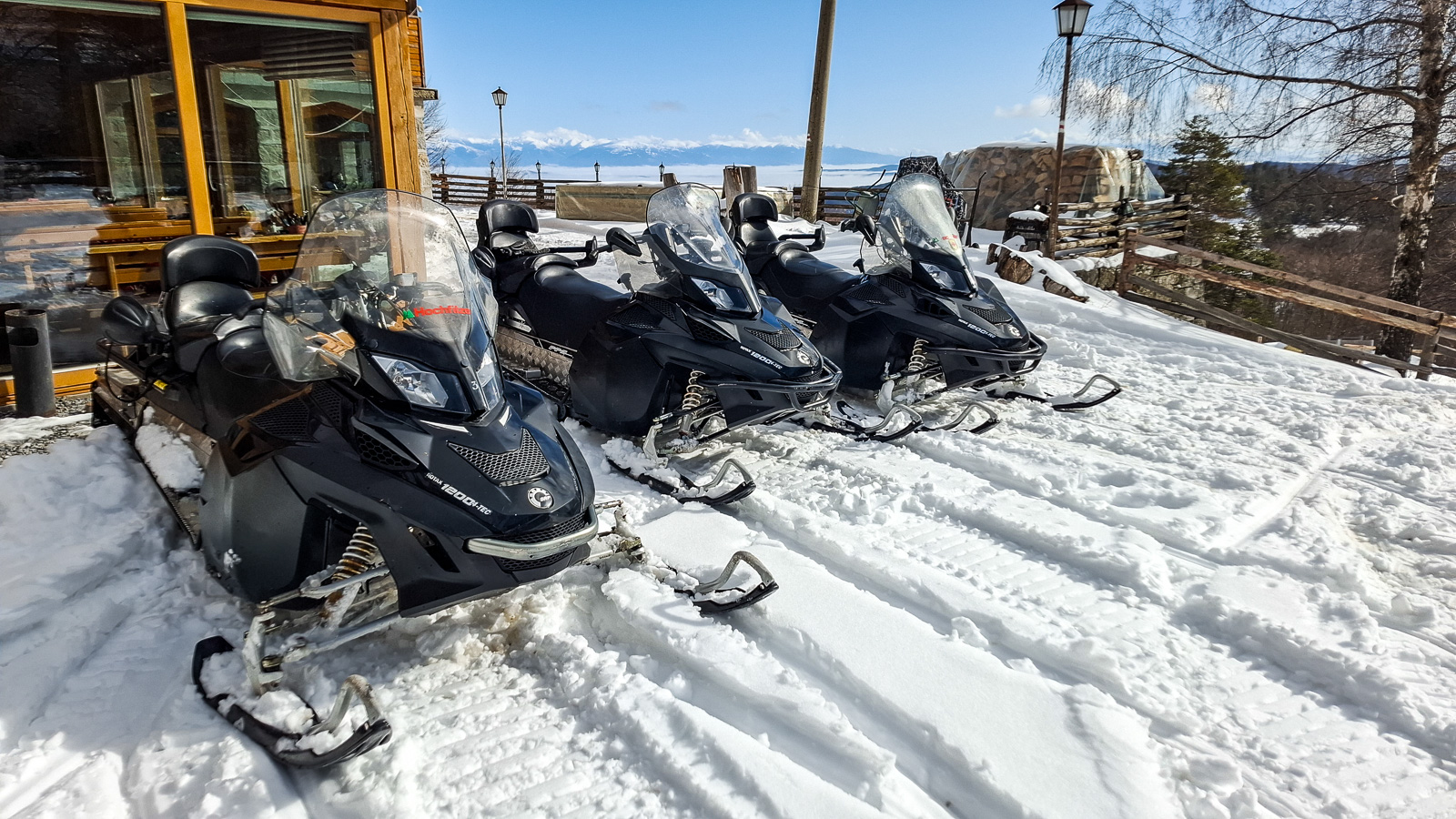 3 snowmobiles on snow with a panoramic mountain view