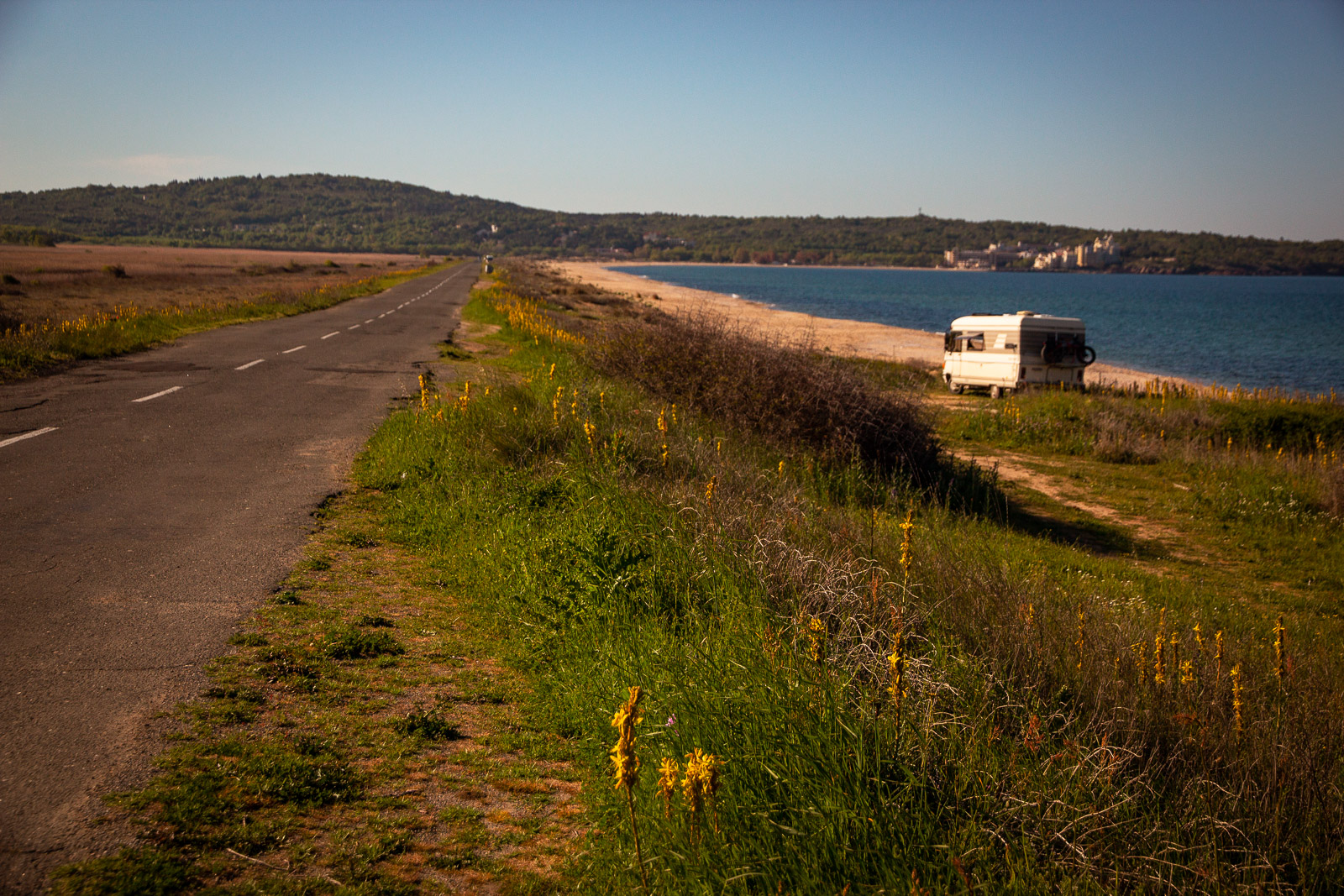 a long road along a black sea beach with a parked caravan