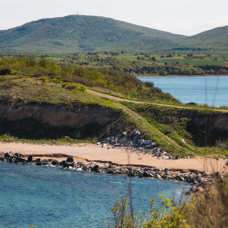 A scenic coastline with a grassy hill leading to a rocky beach, bordered by clear blue water