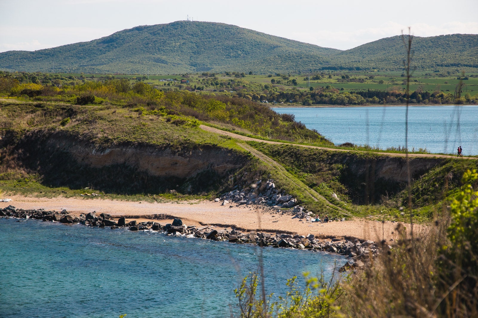 A scenic coastline with a grassy hill leading to a rocky beach, bordered by clear blue water