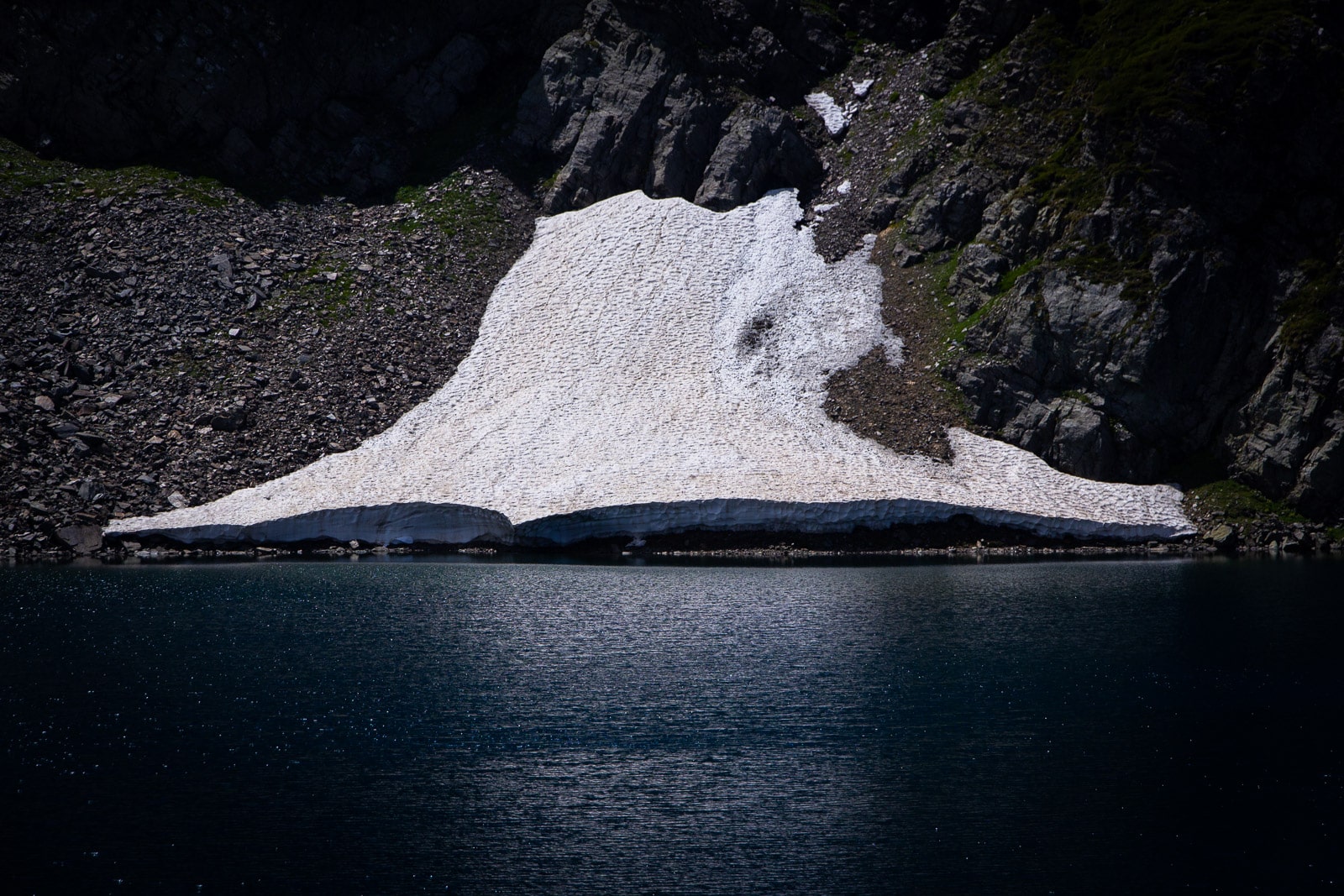 Snow melting into a dark blue lake